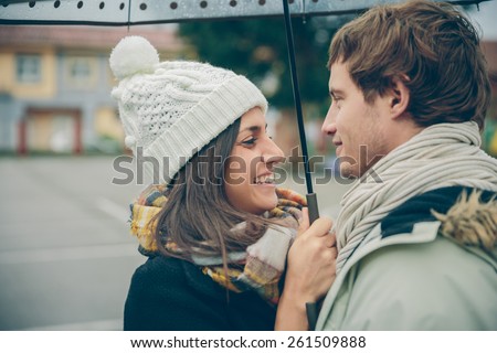 Closeup of young beautiful couple embracing and laughing under the umbrella in an autumn rainy day. Love and couple relationships concept.