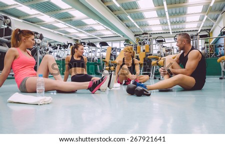 Group of friends talking sitting on the floor of a fitness center after hard training day