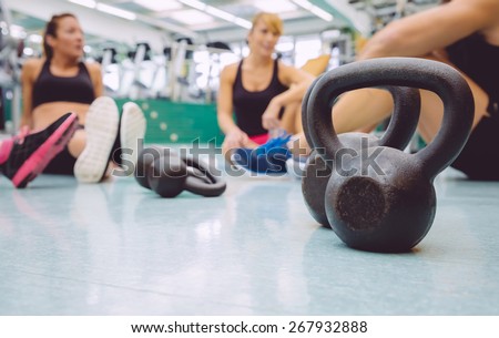 Closeup of black iron kettlebell and people group sitting on the floor of a fitness center in the background