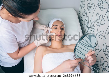 Female doctor showing to young pretty woman the face zones to apply clinic treatment. Medicine, healthcare and beauty concept.