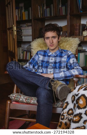 Portrait of serious young man with blue plaid shirt and jeans sitting on a rocking chair at home