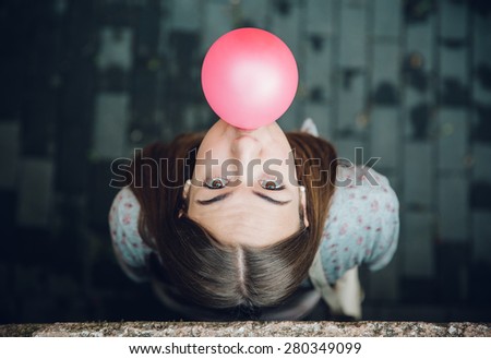 Top view of beautiful young brunette teenage girl blowing pink bubble gum