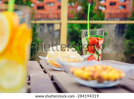 Infused fruit water cocktails and snacks bowls over a wooden table outdoors. Healthy organic summer drinks concept.