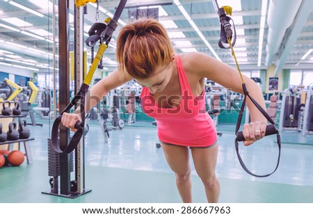 Portrait of beautiful woman doing hard suspension training with fitness straps in a fitness center. Healthy and sporty lifestyle concept.