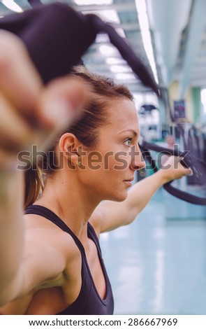 Closeup of beautiful woman doing hard suspension training with fitness straps in a fitness center. Healthy and sporty lifestyle concept.