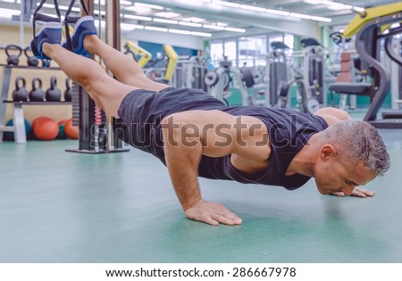 Handsome man doing hard suspension training with fitness straps in a fitness center. Healthy and sporty lifestyle concept.