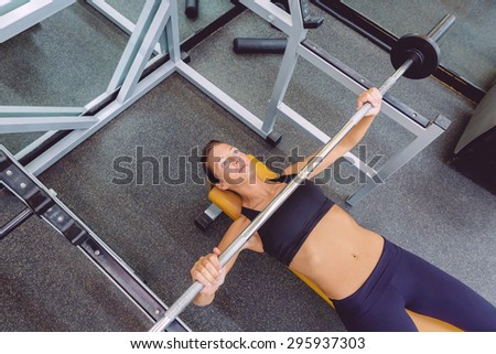 Beautiful woman doing exercises with barbell on a bench press training in a fitness center