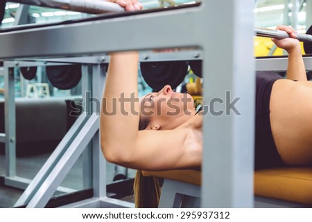Closeup of beautiful woman doing exercises with barbell on a bench press training in a fitness center