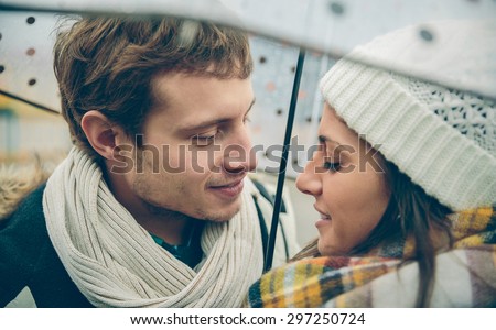 Closeup of young beautiful couple looking at each other with love under the umbrella in an autumn rainy day. Love and couple relationships concept.