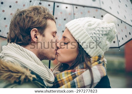 Closeup of young beautiful couple kissing under the umbrella in an autumn rainy day. Image focused on the lips.