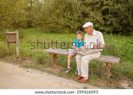 Senior man and cute child reading a newspaper sitting on park bench. Two different generations concept.