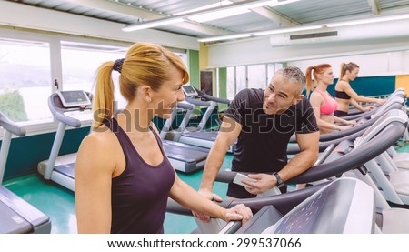 Beautiful fitness woman in a treadmill talking with handsome man on a fitness center