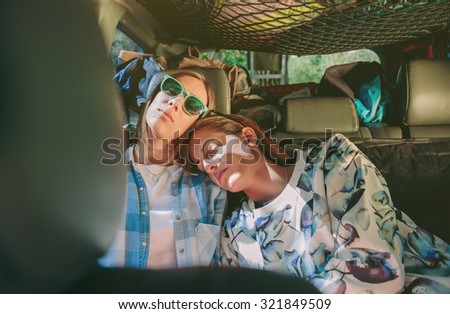 Two tired young women friends sleeping together in the rear seat of car. Female friendship and leisure time concept.