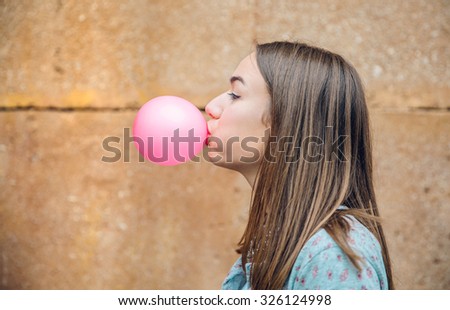 Closeup of beautiful young brunette teenage girl blowing pink bubble gum over a stone wall background