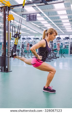 Beautiful woman doing hard suspension training with fitness straps in a fitness center. Healthy and sporty lifestyle concept.