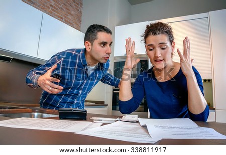 Angry young couple shouting in a hard quarrel by their many debts at home. Financial family problems concept.