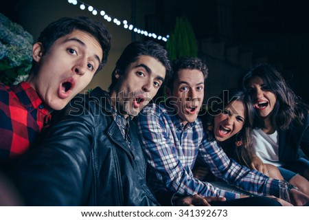 Group of funny young friends shouting while taking a selfie photo in a outdoors party. Friendship and celebrations concept.