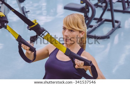 Portrait of beautiful woman doing hard suspension training with fitness straps in a fitness center. Healthy and sporty lifestyle concept.