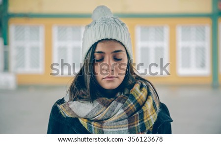 Portrait of young beautiful girl with closed eyes wearing hat and scarf in an autumn rainy day