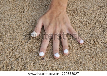 Hand in the sand and shells on nails