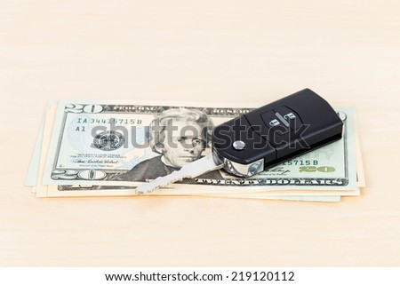 Modern car key and dollar banknote on wooden background