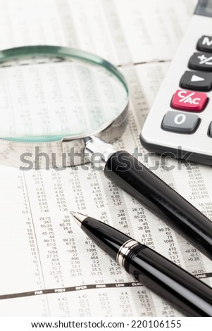 Pen, calculator, and magnifier rest on stock price detail financial newspaper