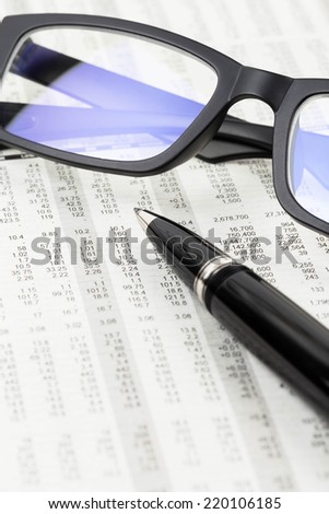 Pen and glasses rest on stock price detail financial newspaper