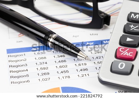 Sales report analysis with pen, calculator, and glasses