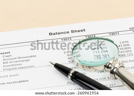 Balance sheet financial report with pen, and magnifier; document is mock-up