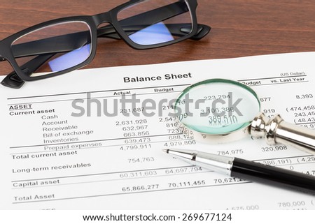 Balance sheet financial report with glasses, and magnifier; document is mock-up