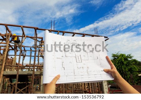 architecture drawings in hand on house building background with blue sky;