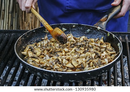 A cook who cooks mushrooms in a pan on the grill.