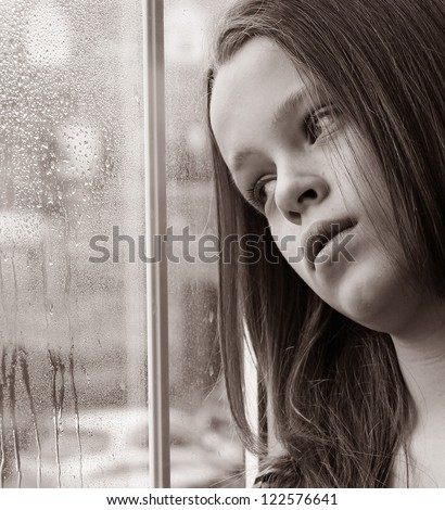 Stunning photo of a young girl gazing through a rainy window