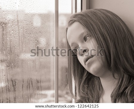 Beautiful close-up of a young girl gazing out of a window on a rainy day