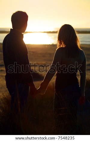 stock photo : A young couple on the beach holding hands at sunset