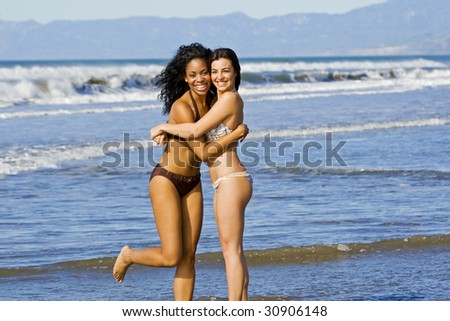Two happy beautiful diverse friends playing on the beach