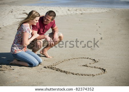 Loving couple at the beach drawing a heart in the sand