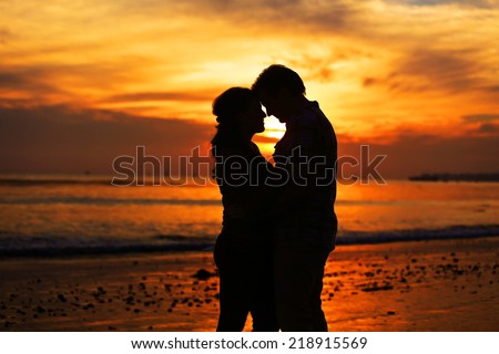Silhouette of a young couple kissing at the beach with the sun
