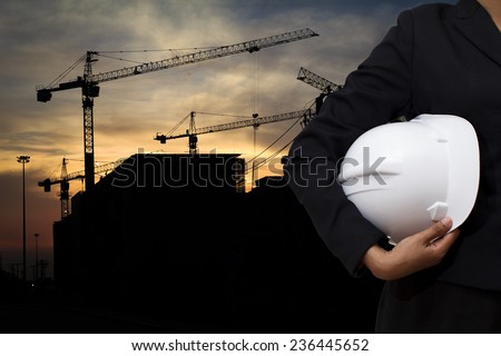 engineer holding white helmet for workers security on background of building construction