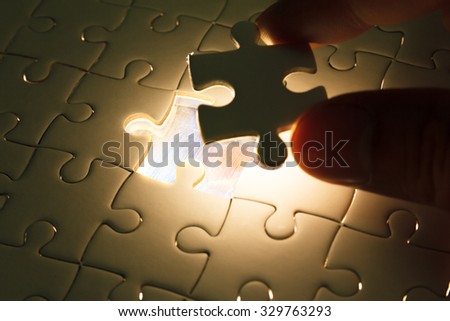 Hand insert missing jigsaw puzzle piece with light glow, business concept for completing the final puzzle piece