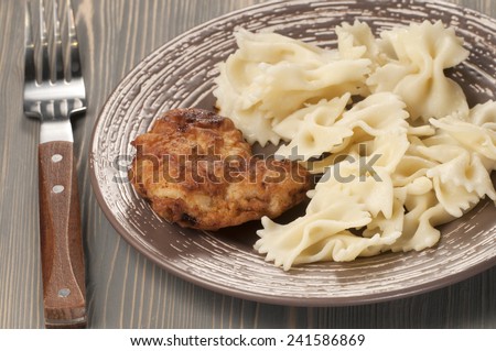 Chicken meat with pasta farfalle on a ceramic plate, closeup