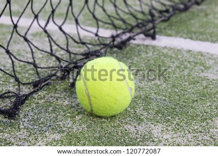 Tennis or paddle ball on synthetic grass of paddle court with net on the background