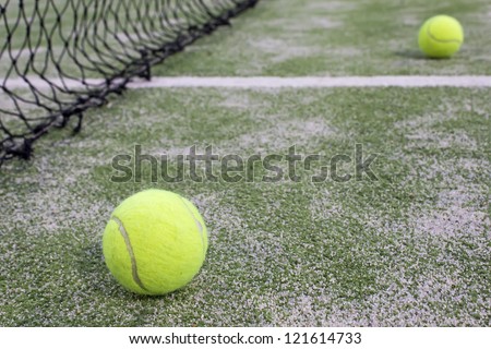 Tennis or paddle balls on synthetic grass of paddle court with net on the background