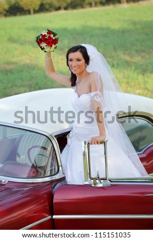 Wedding, beautiful bride on vintage car wave with bouquet of red roses