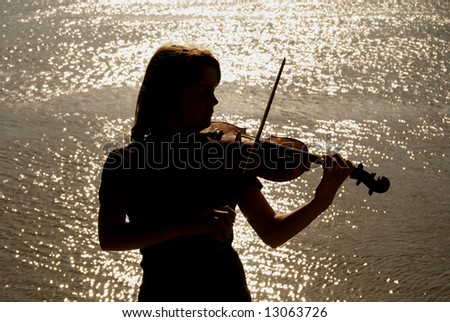 Silhouette of teenage violin player over sunset on river,lake or sea