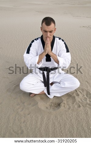 Young man martial art master meditating  at sand