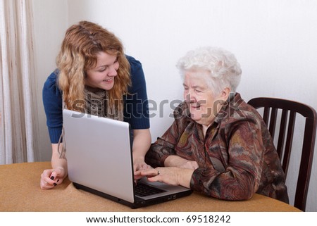 Young girl teaching senior woman to work at computer