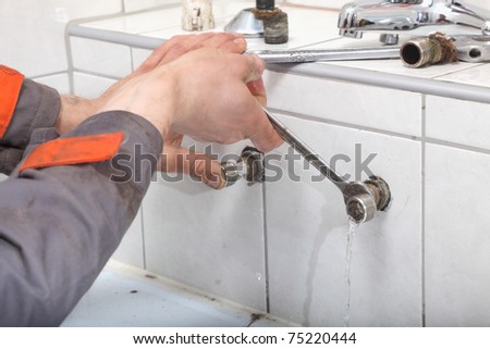 Plumber hands fixing water pipe with spanner and with leaking water from pipe