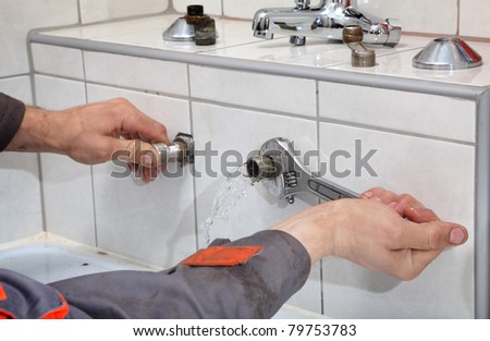 Plumber hands fixing water pipe with spanner and with leaking water from pipe
