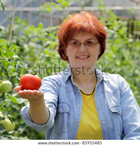 Smiling caucasian woman holding tomato in  hand, selective focus on tomato